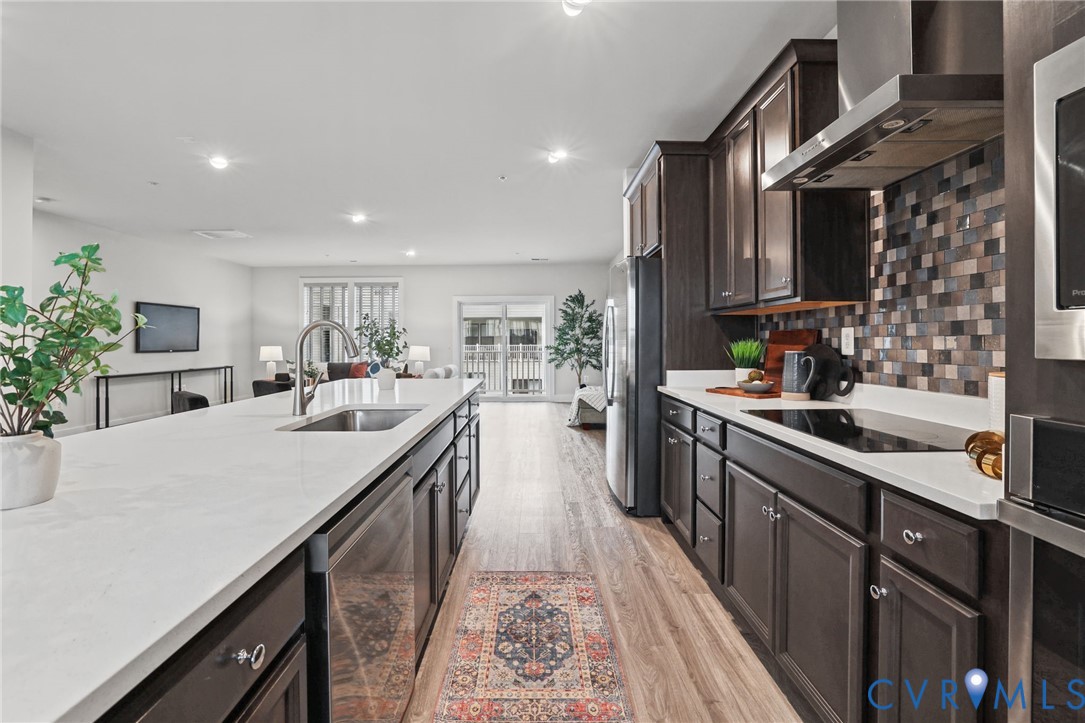 Kitchen featuring dark cabinetry, expansive quartz countertops, stainless steel appliances, a mosaic tile backsplash, and wood-finish flooring