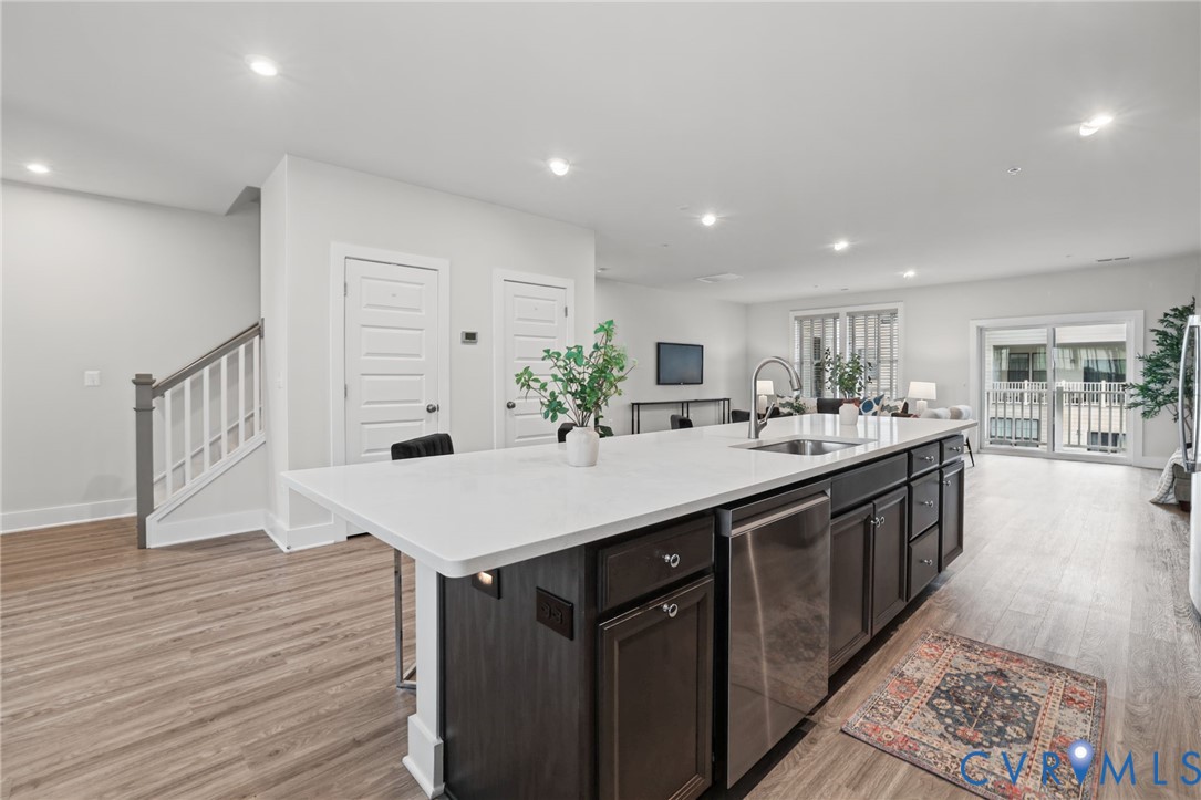 Kitchen island with stone-finish countertop, stainless steel undermount sink, dark-finish cabinetry, recessed lighting, and wood-finish flooring