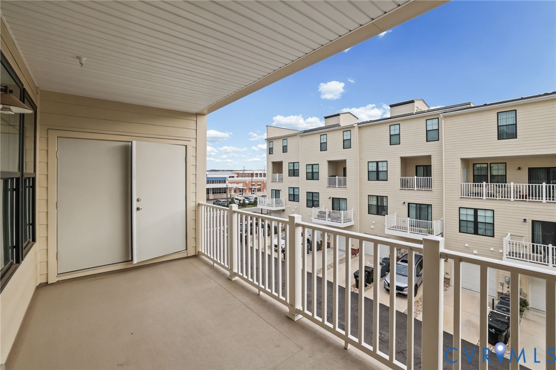 Covered balcony featuring concrete flooring, white picket-style railings, and double-door access