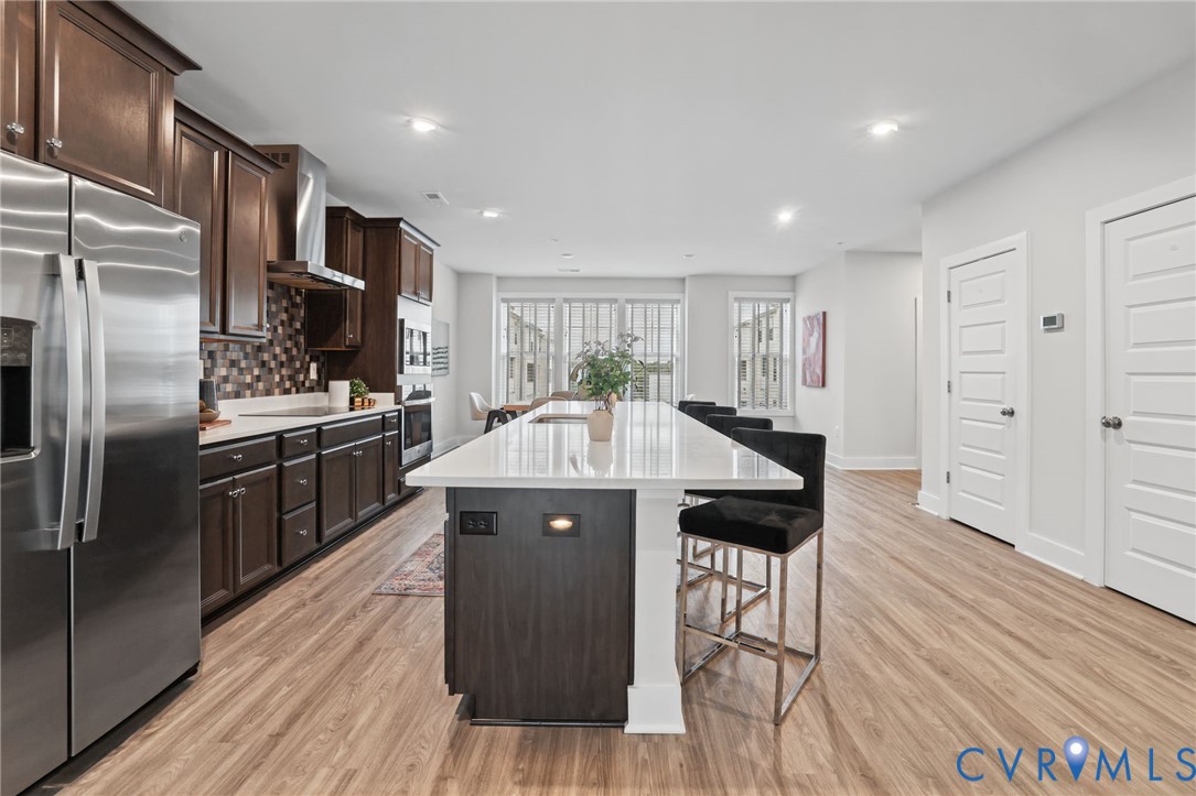 Kitchen featuring an expansive center island with a quartz countertop, dark wood-finish cabinetry, stainless steel appliances, and wood-finish flooring