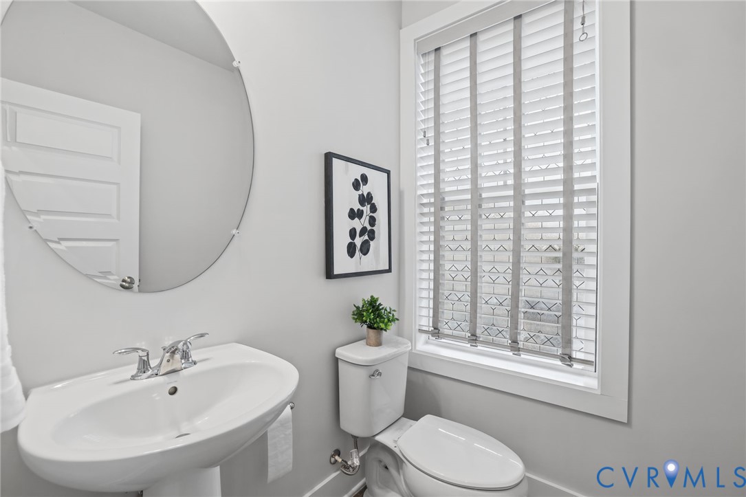 Pedestal sink with polished chrome dual-handle faucet, oval frameless wall mirror, and window with built-in slatted blinds