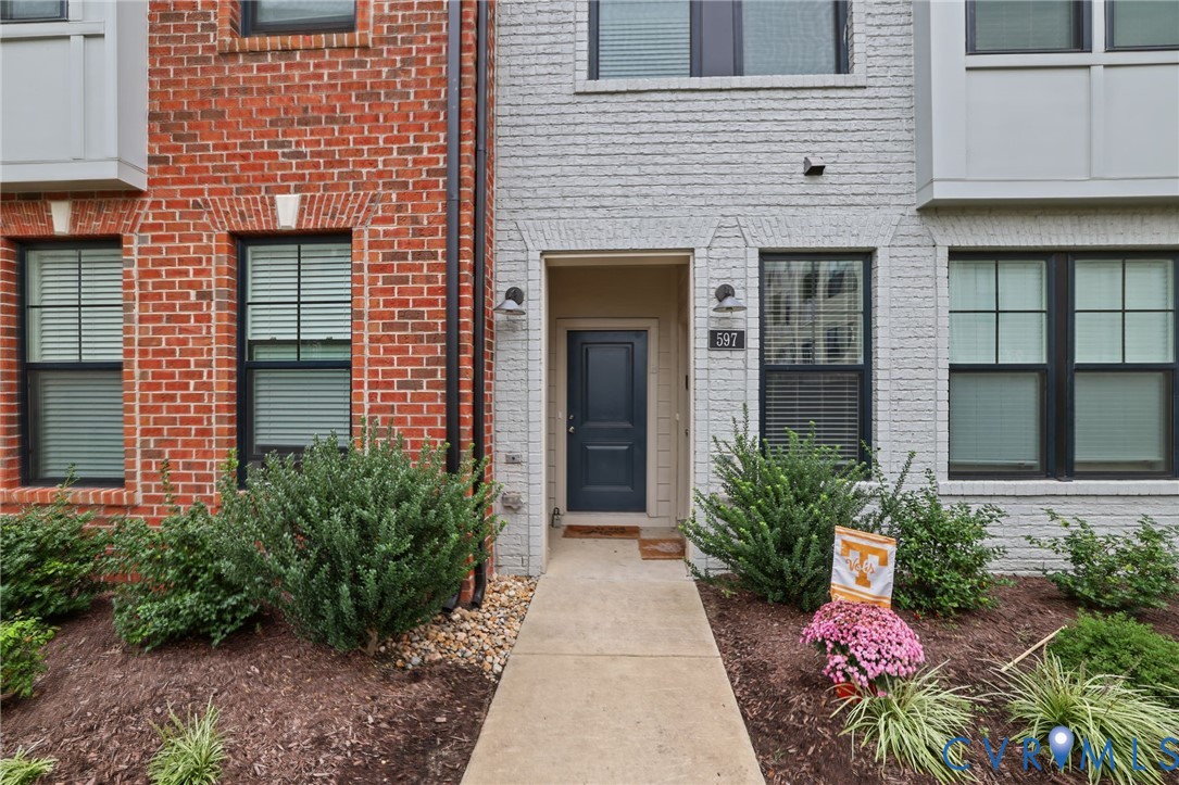 Exterior facade featuring red and white brick masonry, a concrete walkway, multi-pane windows with dark frames, and an entry door with a multi-panel design