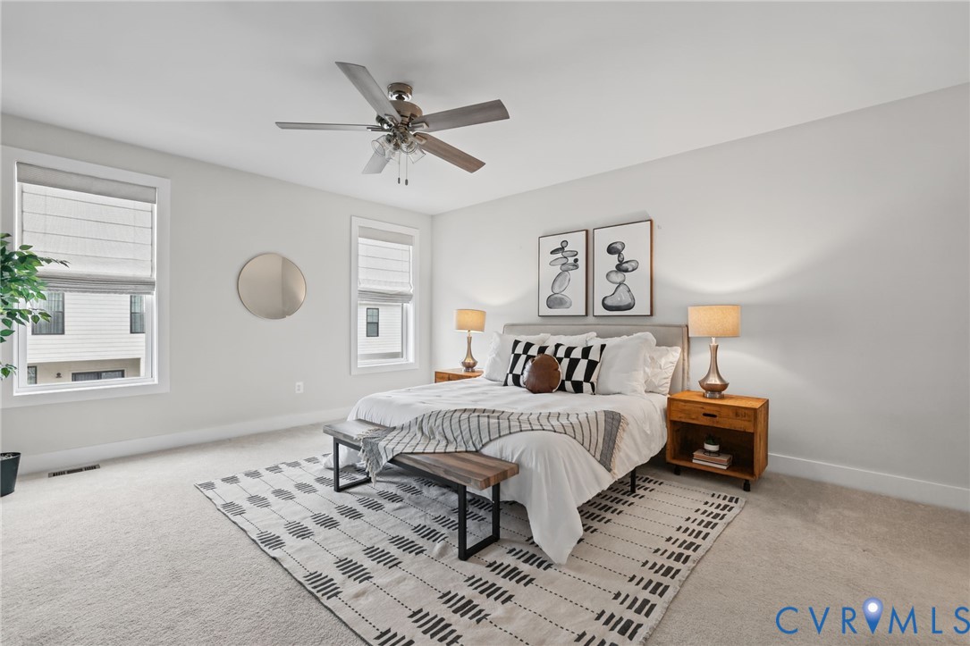 Neutral wall-to-wall carpeting, two dual-pane windows with fitted shades, and a ceiling fan with integrated lighting
