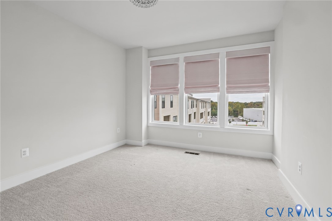 Room featuring wall-to-wall carpeting and a triple-window configuration with installed fabric shades and overhead crystal-style light fixture