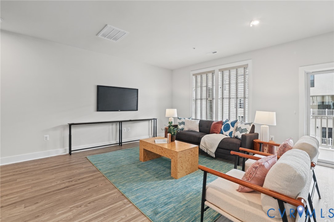 Living area featuring wood-finish flooring, neutral wall tones, recessed lighting, and large windows with horizontal blinds
