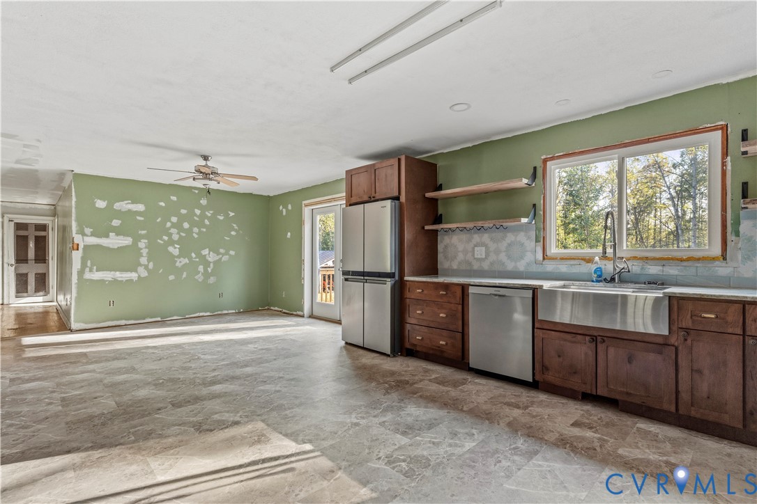Stainless steel appliances, wood-finish cabinetry, farmhouse sink, decorative tile backsplash, and open shelving