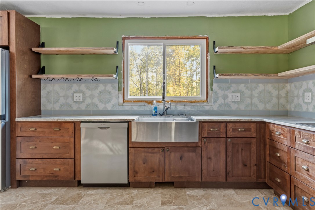 Kitchen featuring wood cabinetry, stainless steel apron-front sink, light-toned countertops, and patterned tile backsplash