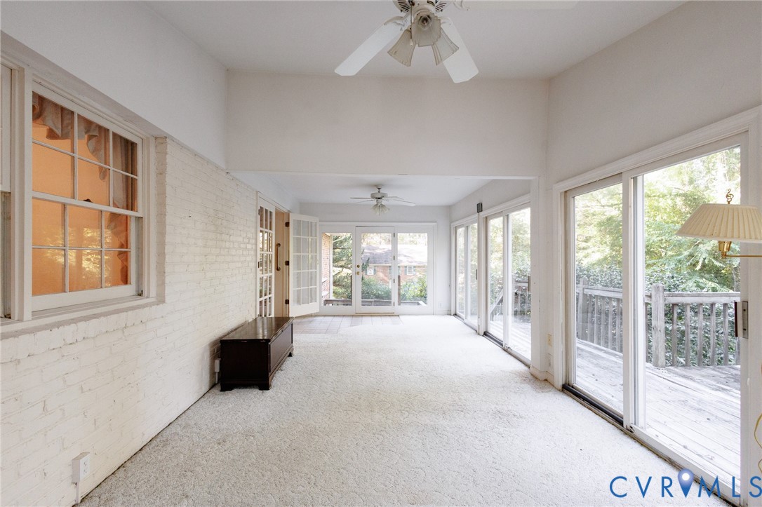 Sunroom featuring white painted brick walls, multi-panel sliding glass doors, double glass-pane doors, and dual ceiling fans