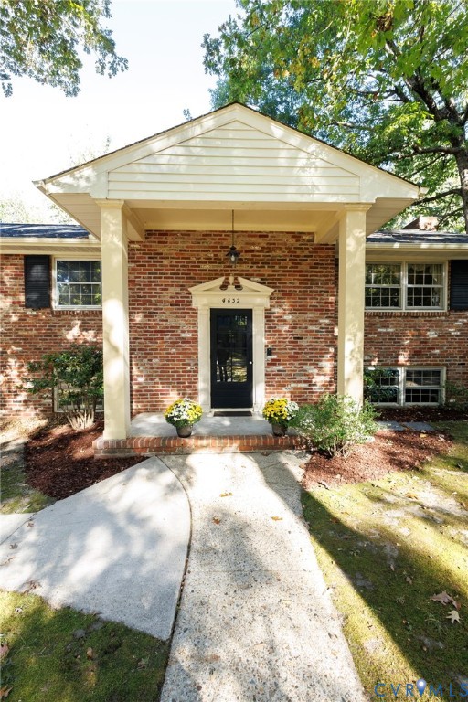 Brick exterior featuring a covered entryway with square columns, a pediment door surround, and multi-pane windows with dark shutters