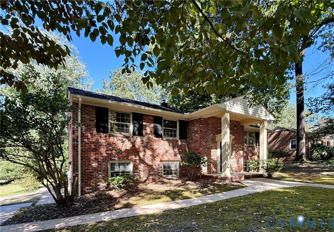 Brick exterior featuring a covered front porch with columns, shuttered windows, and a paved walkway