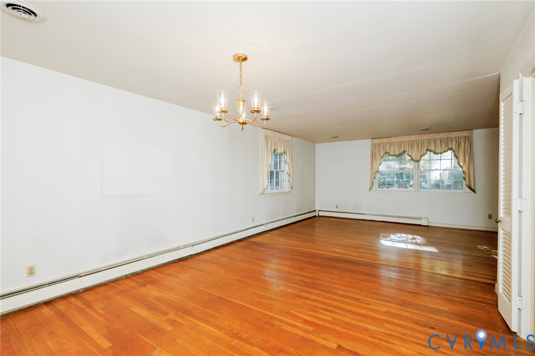 Expansive interior space featuring wood-finish flooring, a multi-arm chandelier, and two windows with double-hung frames