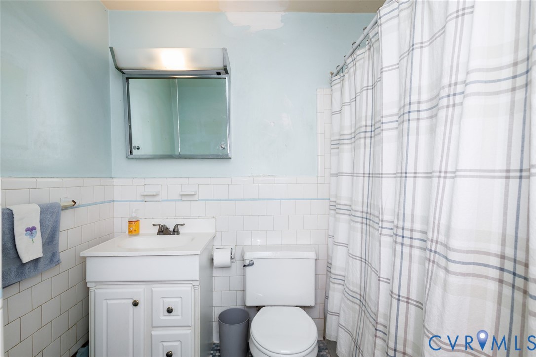 Bathroom featuring white subway tile wall cladding, vanity with integrated basin and storage cabinetry, medicine cabinet with surface-mounted lighting, and a bathtub enclosure