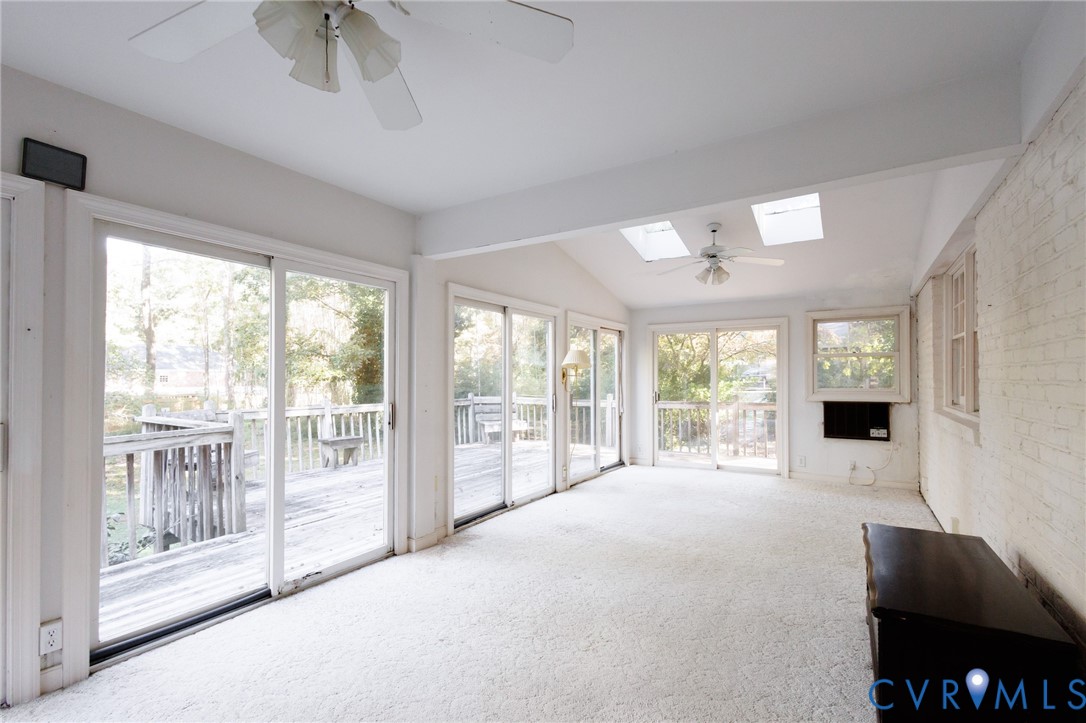 Sunroom featuring multiple sliding glass doors, exposed brick wall, dual skylights, and ceiling fans