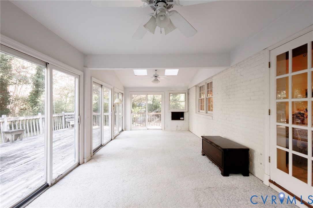 Sunroom featuring a white painted brick wall, dual skylights, multiple sliding glass doors, ceiling fans, and a multi-pane glass door
