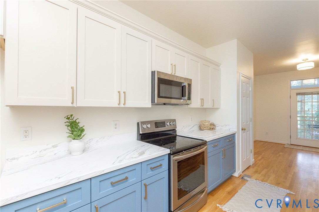 Kitchen featuring white upper cabinetry, blue lower cabinetry, stone-patterned countertops, stainless steel appliances, and wood-finish flooring
