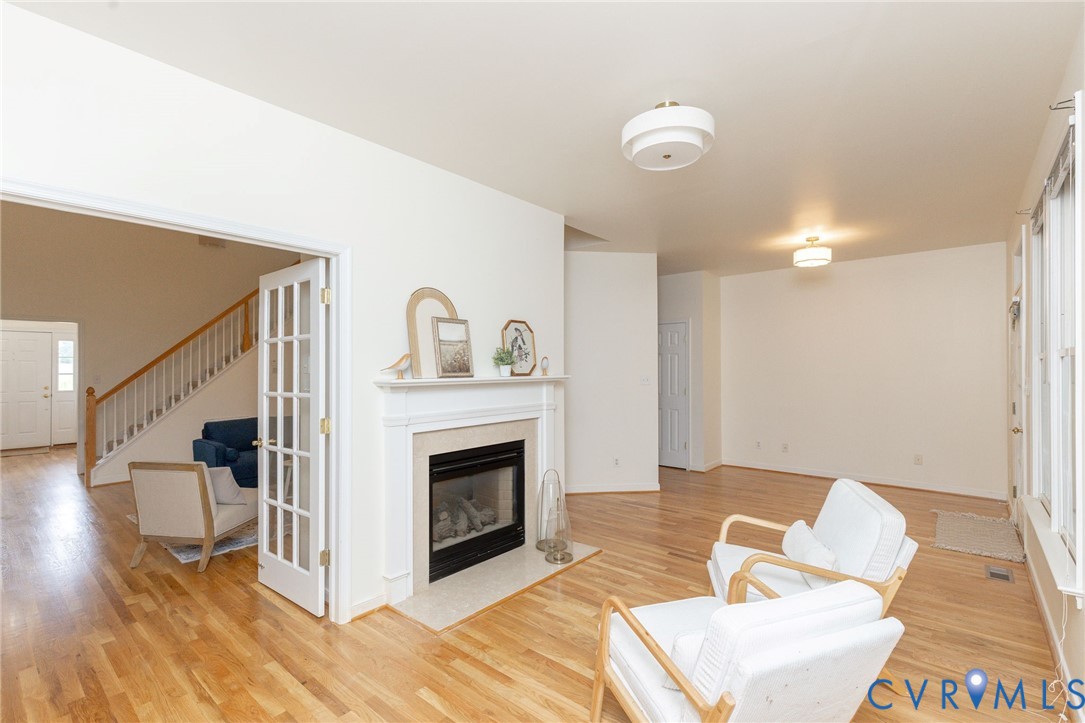 Living area featuring wood-finish flooring, a fireplace with a stone-surround and mantle, French doors, and ceiling-mounted drum lighting