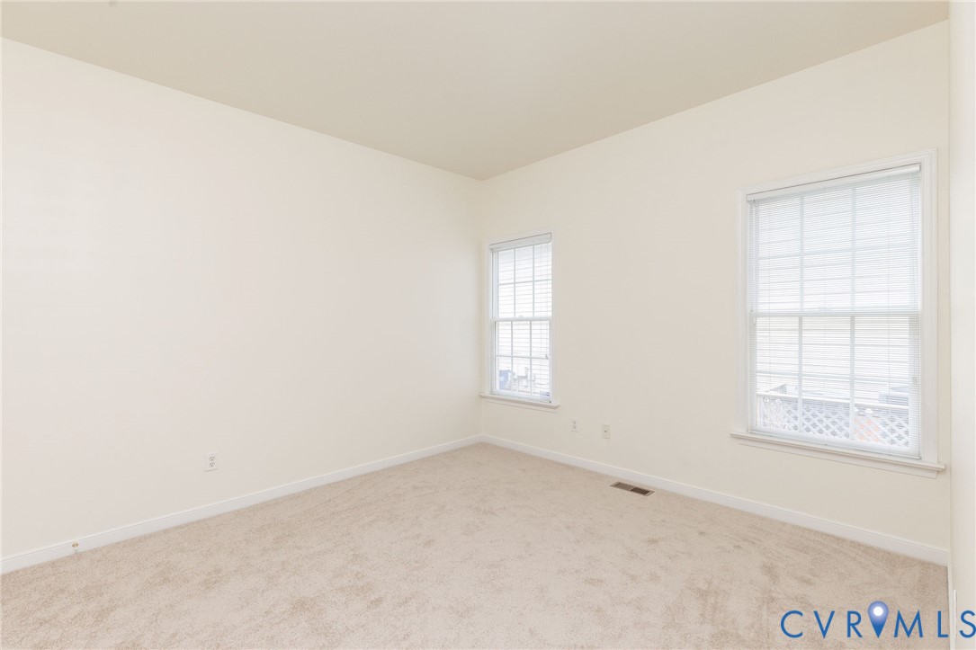 Neutral-toned interior space featuring light-colored wall-to-wall carpeting, high ceilings, and dual windows with white gridded panes