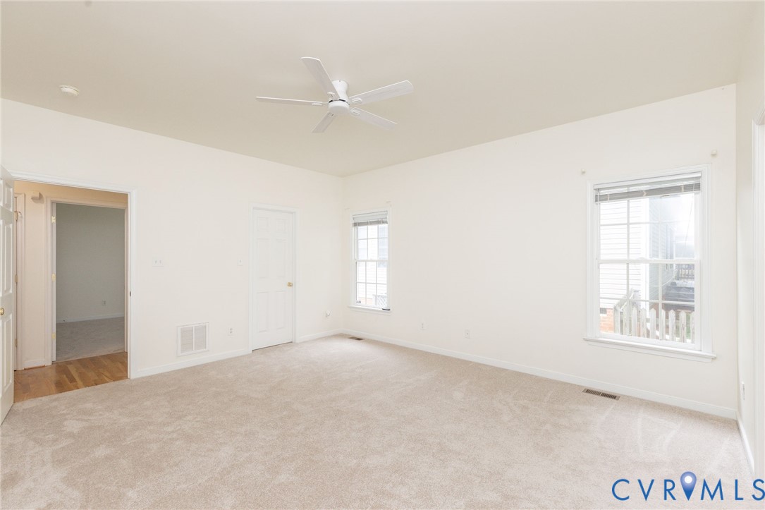 Neutral-toned carpeted interior featuring a ceiling fan, multiple windows with blinds, and solid-core paneled doors