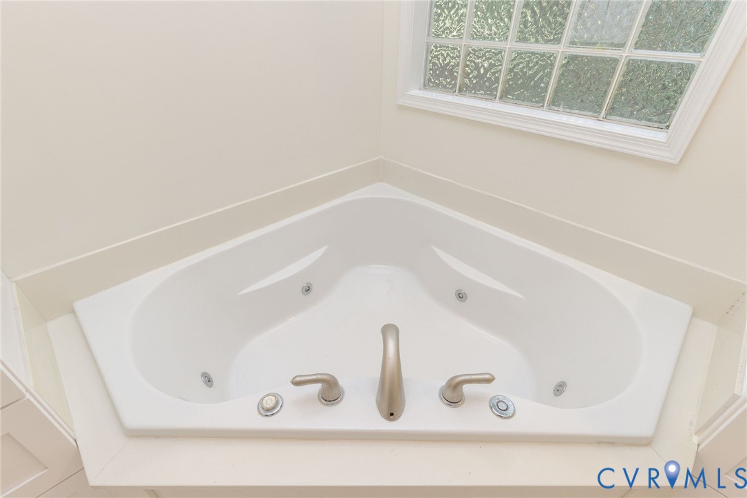 Corner soaking jetted tub featuring a white surround, brushed nickel faucet fixtures, and a framed window with obscured glass