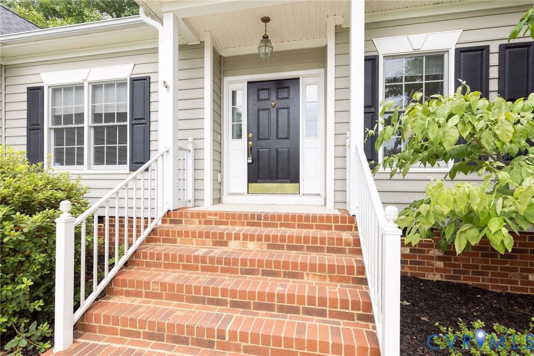 Exterior entry featuring a covered porch, brick steps with white railings, a multi-paneled door with sidelights, and black decorative shutters