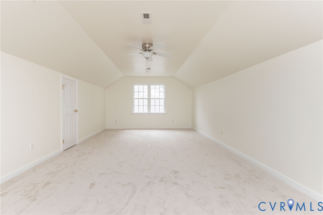 Interior space featuring vaulted ceilings, neutral wall tones, wall-to-wall carpeting, a multi-pane window, and a ceiling fan with integrated light fixture