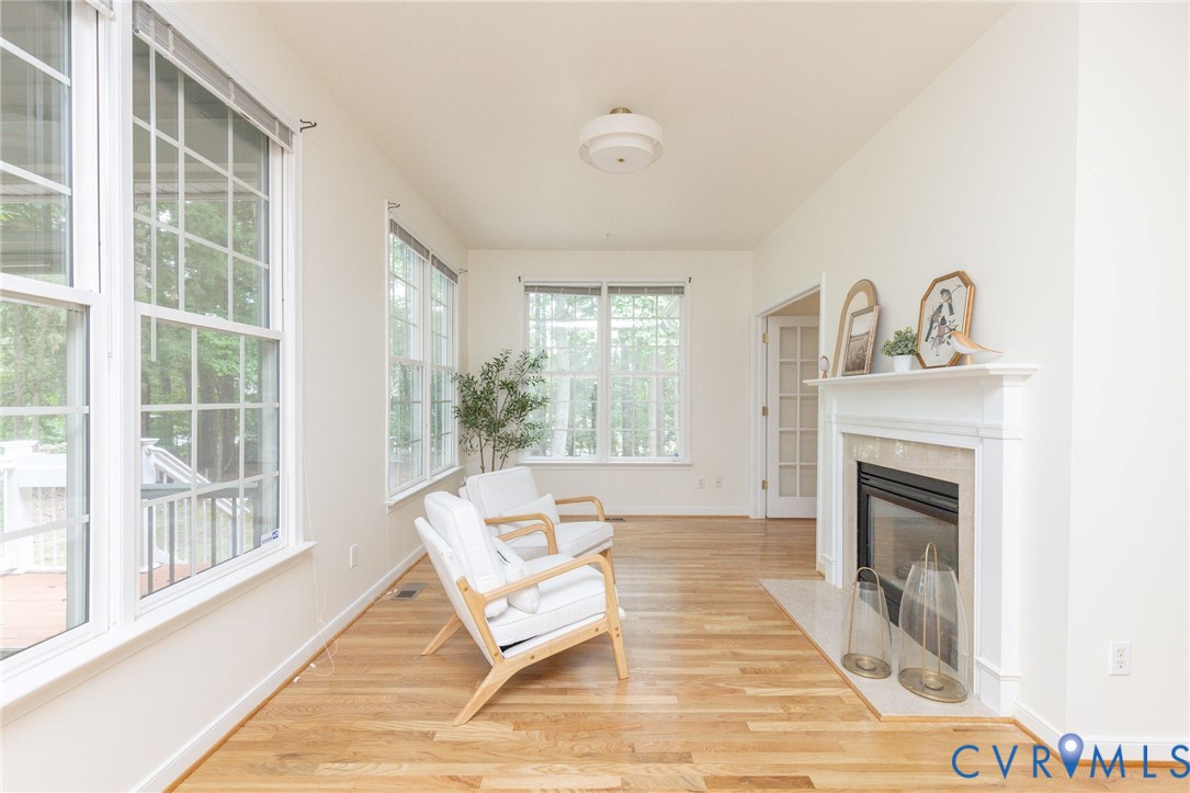 Sunroom featuring wood-finish flooring, multi-pane windows, and a fireplace with a stone surround and white mantle, complemented by a central flush-mount ceiling light