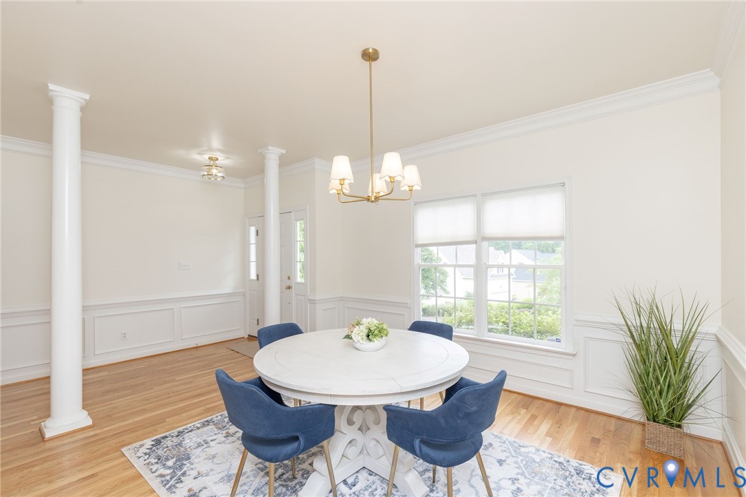 Wood-finish flooring, wainscoting, decorative architectural columns, crown molding, and a multi-arm metallic chandelier