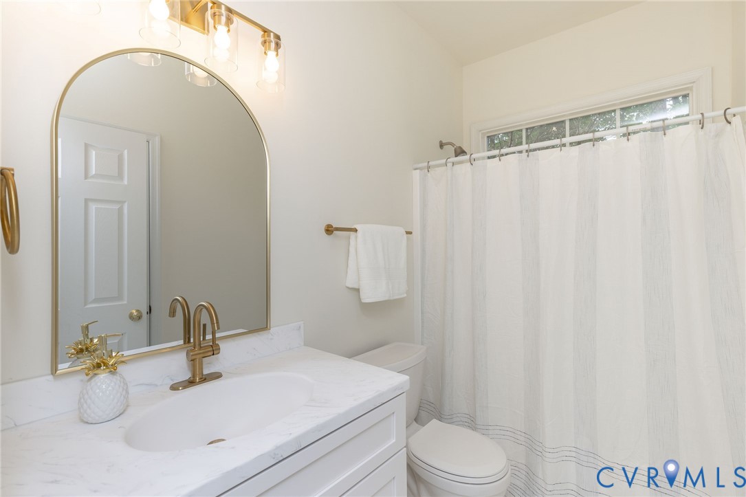 Arched vanity mirror with metallic frame, brass-finish faucet, stone-surfaced countertop, and multi-bulb vanity light fixture