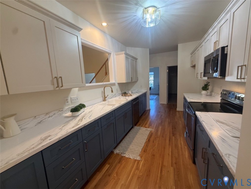 Kitchen featuring dual-tone cabinetry, stone-finish countertops, wood-finish flooring, brass-tone hardware, and built-in stainless steel appliances
