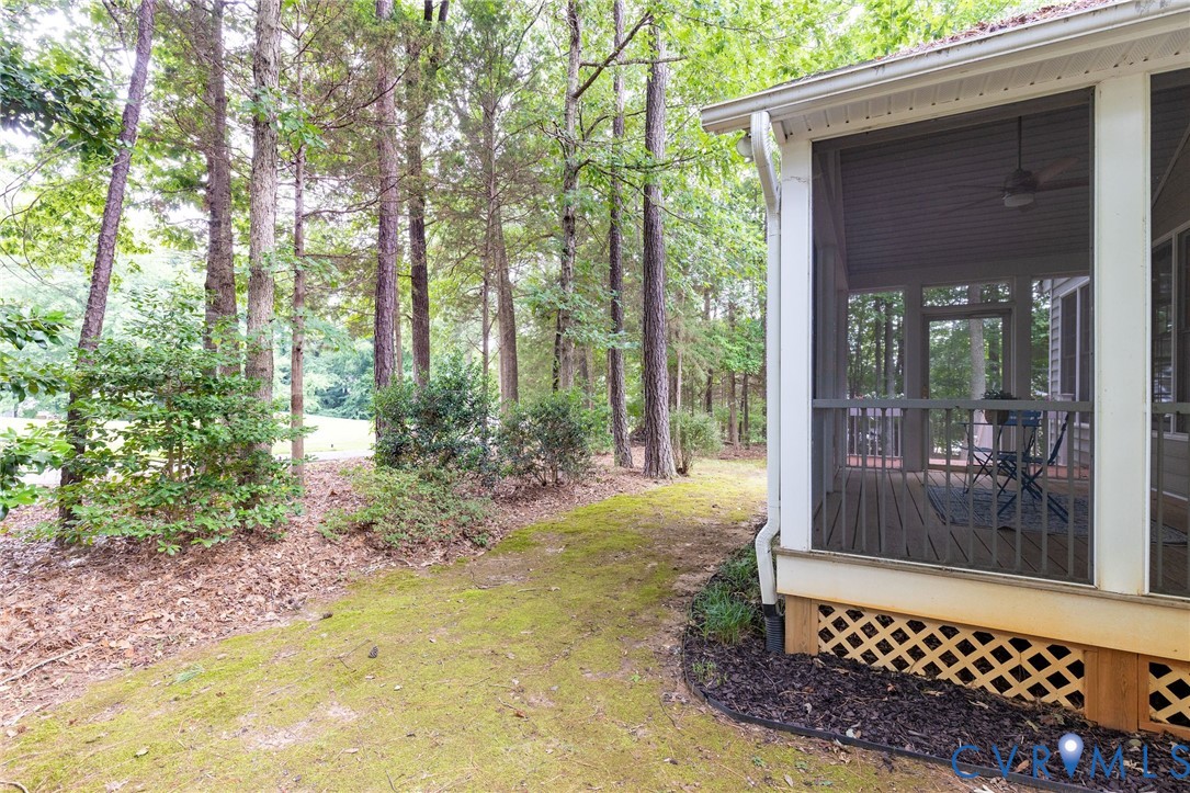 Screened-in porch featuring a ceiling fan and wooden lattice skirting, situated on a lot with mature trees and foliage