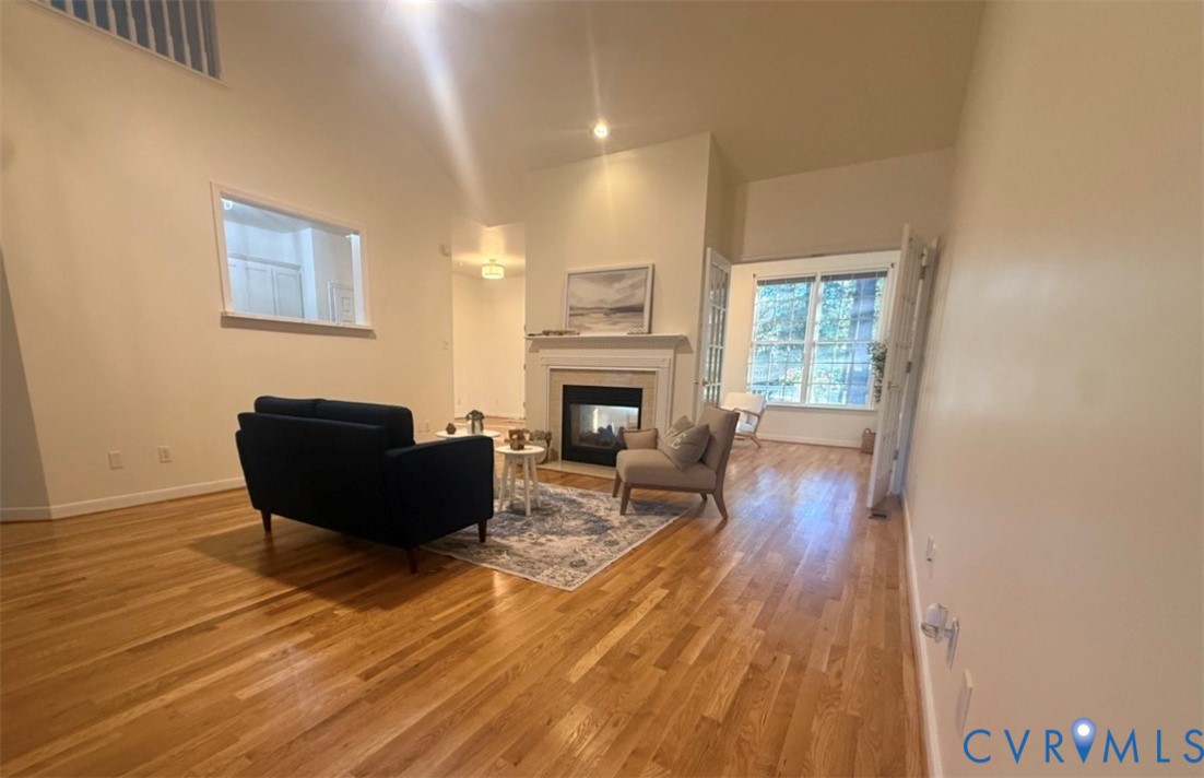 Vaulted ceilings, wood-finish flooring, central fireplace with a mantel, interior pass-through window, and multi-pane glass doors