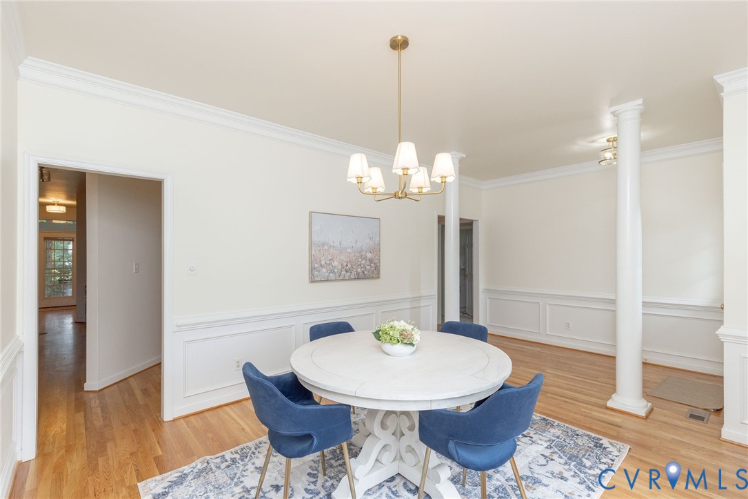 Dining area featuring wood-finish flooring, wainscoting, decorative columns, and a multi-light chandelier