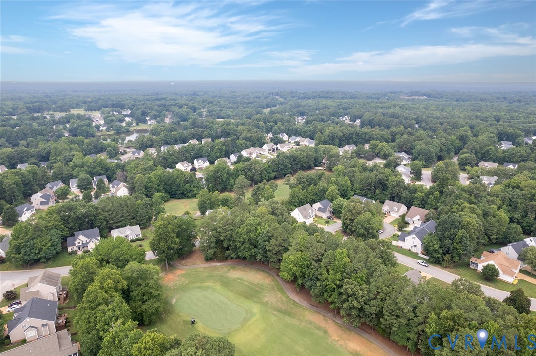 Aerial perspective featuring a manicured golf course green, expansive surrounding woodland, and residential infrastructure