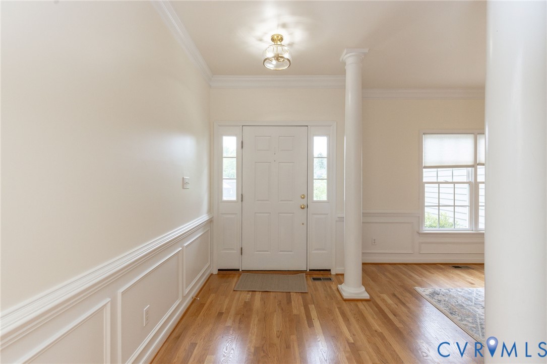 Entryway featuring wood-finish flooring, white panel wainscoting, a column, crown molding, and a multi-pane glass door with side lights