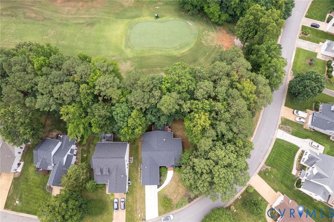 Aerial perspective featuring a residential lot with mature canopy trees, a concrete driveway, and direct proximity to a golf course putting green