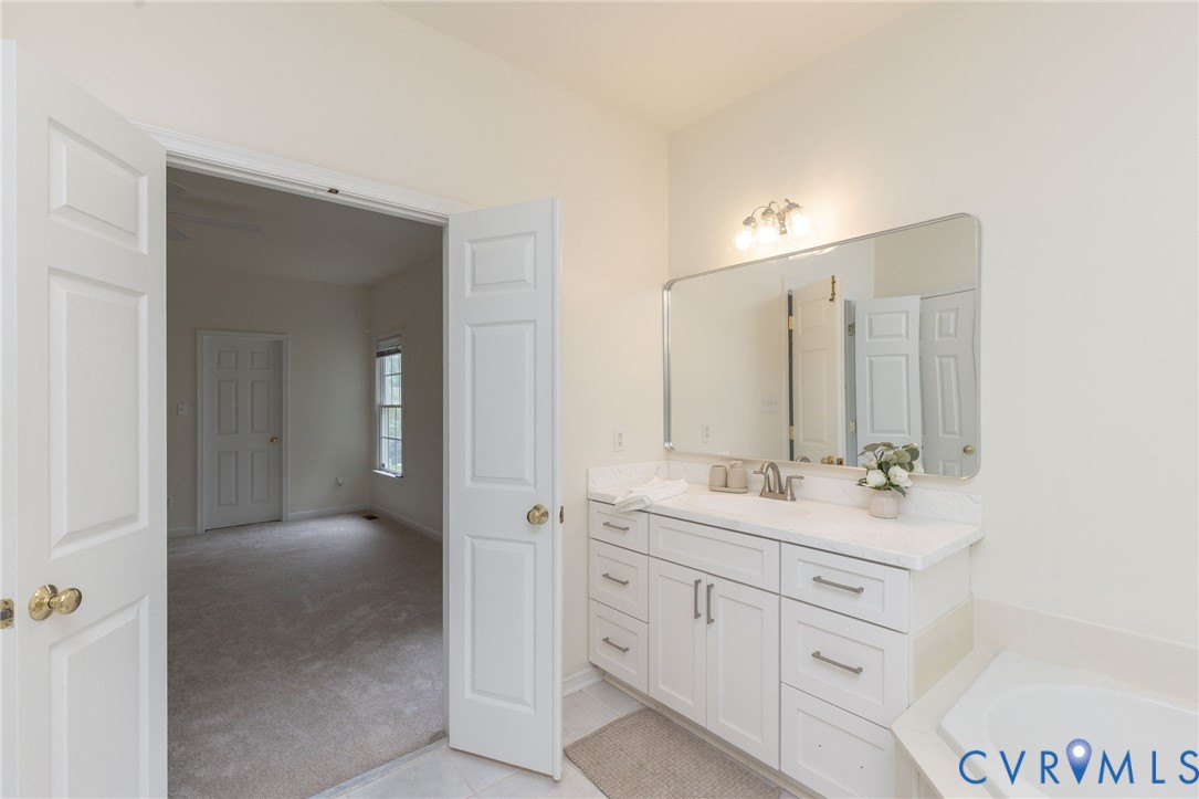 White cabinetry vanity with stone-finish countertop, undermount sink, multi-drawer storage, and large wall-mounted mirror with integrated light fixture