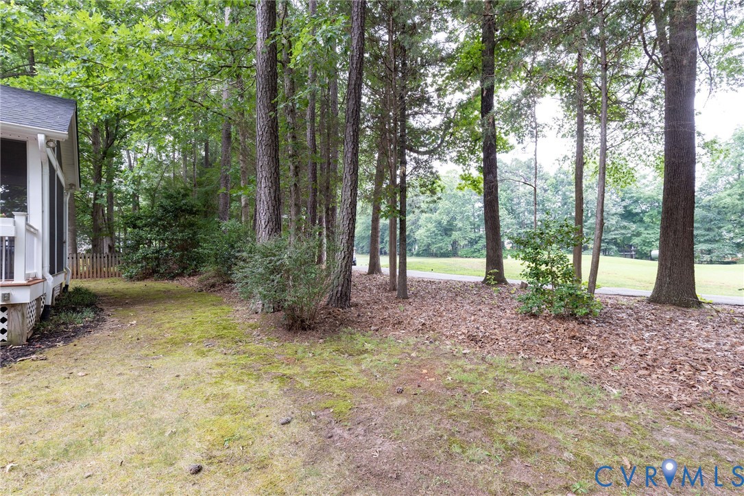Ground-level deck featuring a partial white railing, surrounded by mature trees and established landscaping