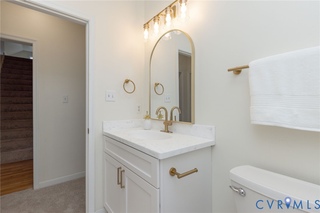 Bathroom vanity featuring a stone-look countertop, white Shaker-style cabinetry, an arched mirror, and brass-finish hardware and lighting fixtures