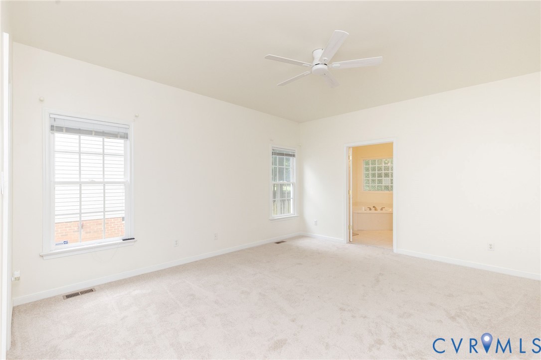 Neutral-toned wall-to-wall carpeting, white-finished walls, two multi-pane windows, and a white ceiling fan with integrated lighting