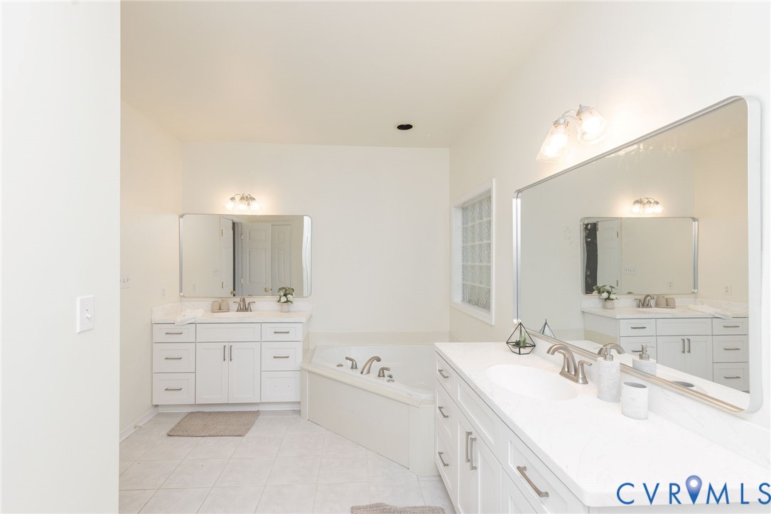 Dual white cabinetry vanities with light-toned countertops, inset sinks, chrome fixtures, large rectangular mirrors, and a corner soaking tub