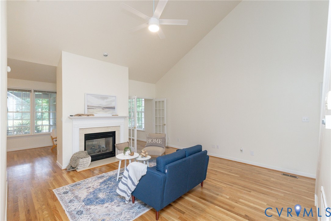 Vaulted ceilings, wood-finish flooring, central fireplace with a classic mantel, and multi-pane glass doors