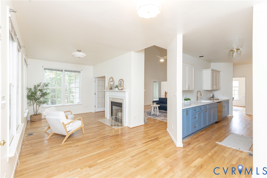 Living area with wood-finish flooring and a fireplace featuring a white mantel, kitchen cabinetry with a two-tone color scheme, quartz countertops, and stainless steel dishwasher