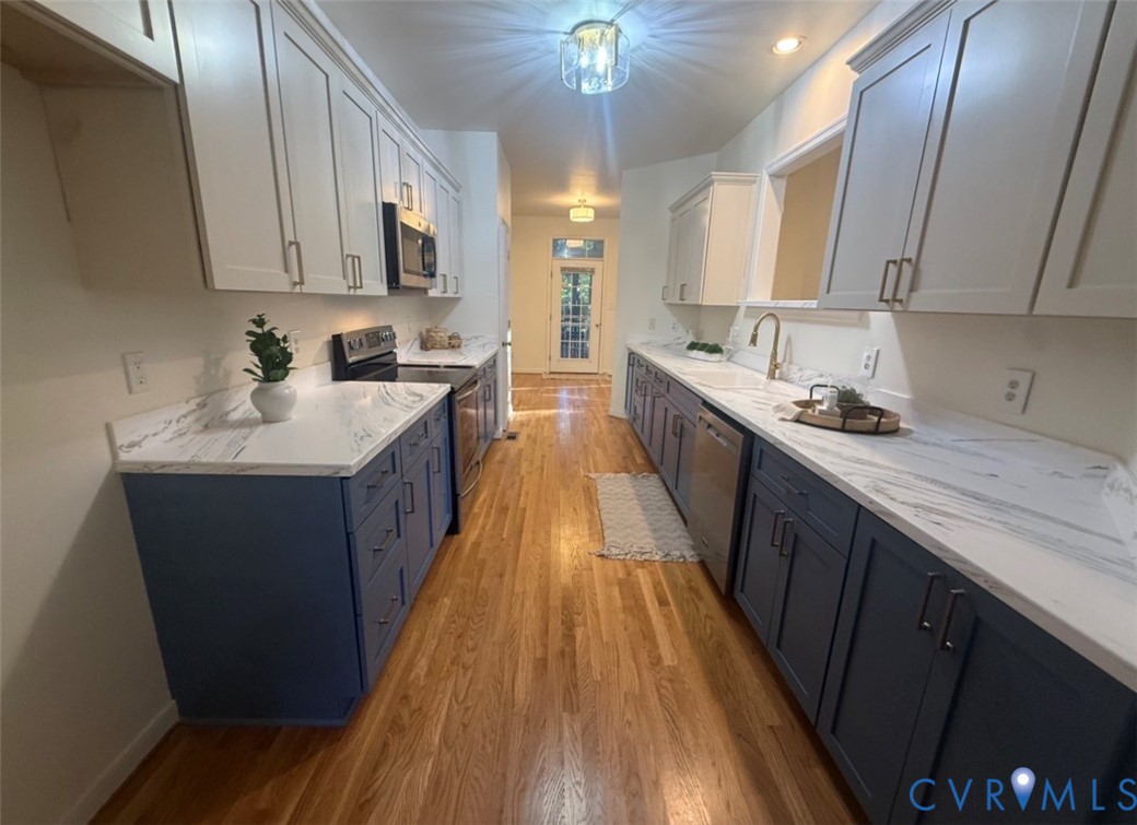 Kitchen featuring two-tone shaker cabinetry, stone-finish countertops, wood-finish flooring, and built-in stainless steel appliances