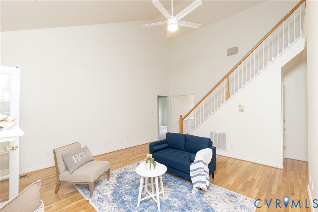 Vaulted ceilings, wood-finish flooring, staircase with a wood handrail and white balusters, and a ceiling fan with integrated lighting