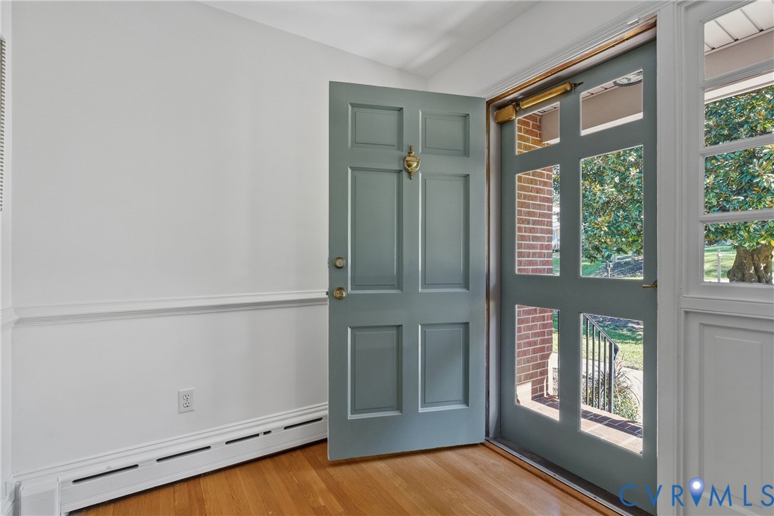 Entryway featuring wood-finish flooring, a six-panel door with a brass-finish knocker, and a glass-paneled storm door