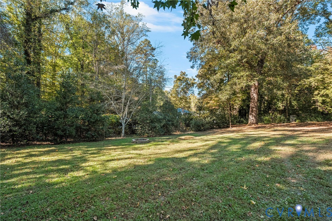 Expansive backyard featuring a lawn, stone fire pit, and perimeter of mature trees