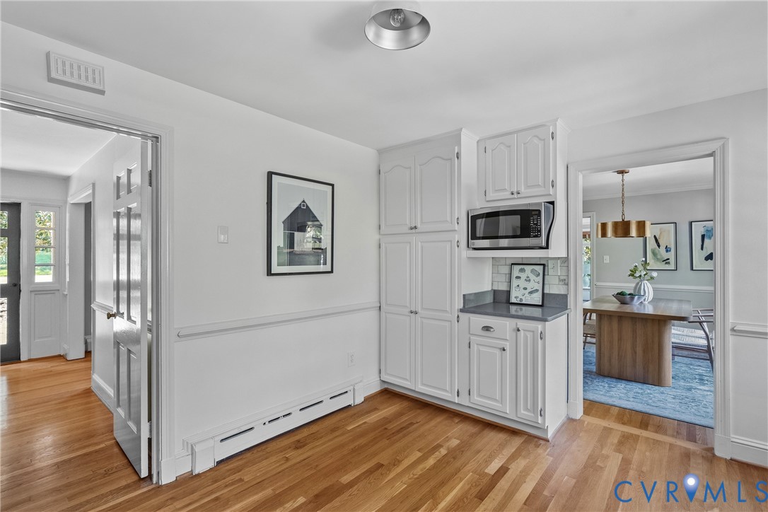 Built-in white cabinetry, integrated microwave, solid surface countertops, tile backsplash, and wood-finish flooring