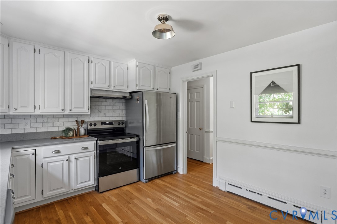Kitchen featuring white cabinetry, subway tile backsplash, stainless steel appliances, wood-finish flooring, and crown-molding details