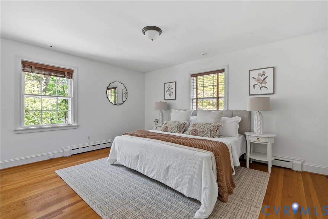 Room featuring wood-finish flooring, two multi-pane windows with horizontal blinds, and a central flush-mount ceiling light fixture