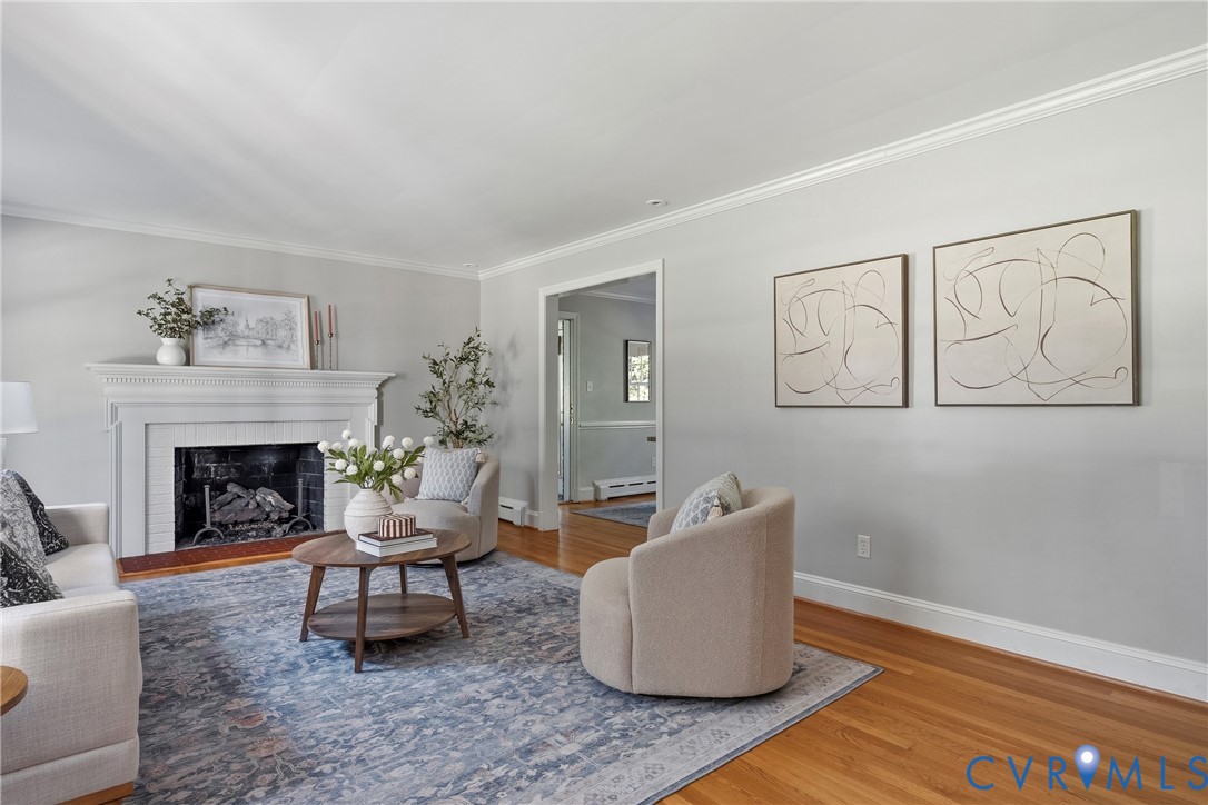 Living area featuring hardwood flooring, crown molding, and a white mantel fireplace with a tile surround